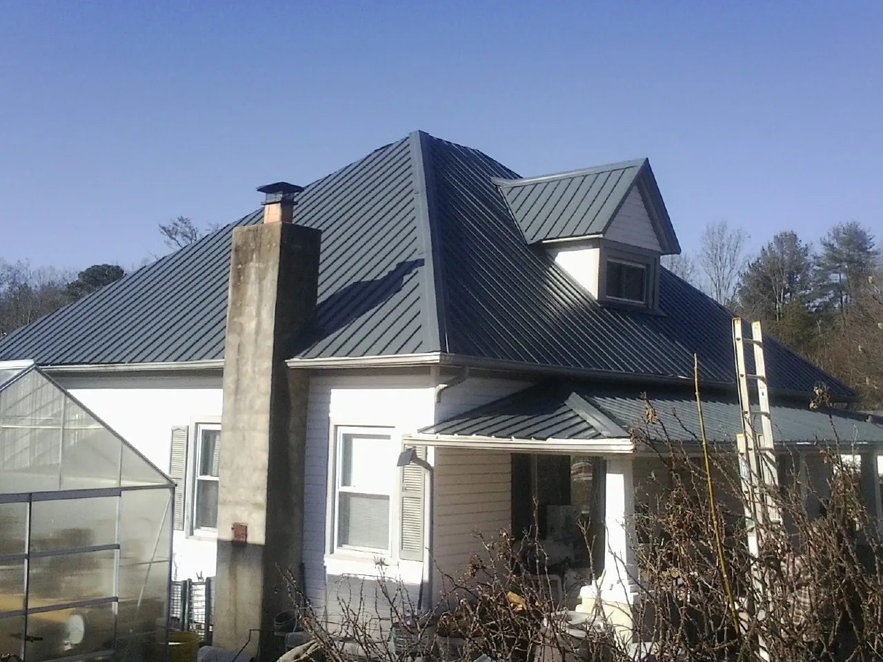 Dark blue standing seam metal roof on a white farmhouse with dormer — Slate & Tile Roof Repair by Roofing Brothers in Gold Creek