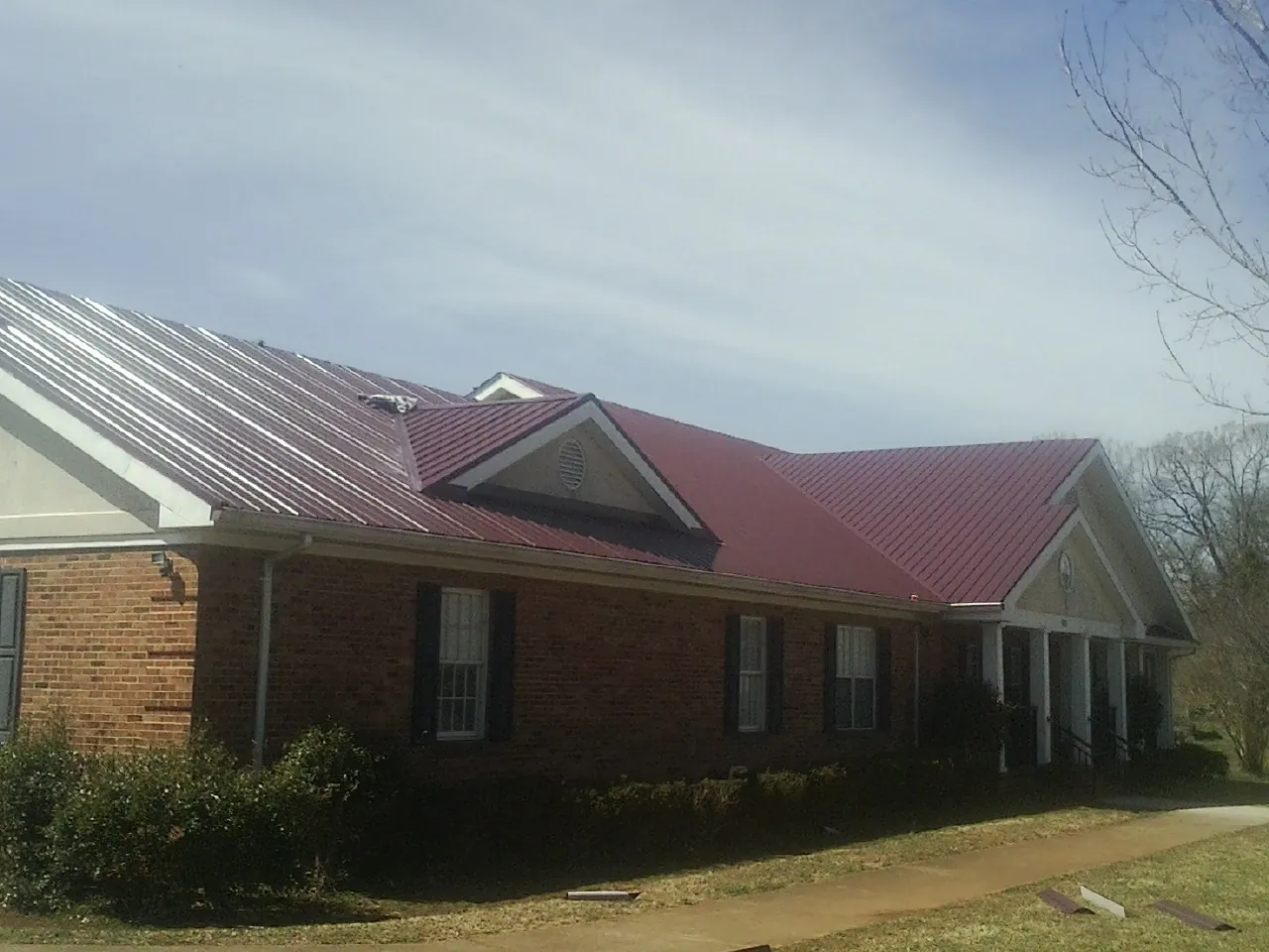 Red metal roof with gabled entries on a long brick building, from a Hail Damage Roof Repair job in Gold Creek
