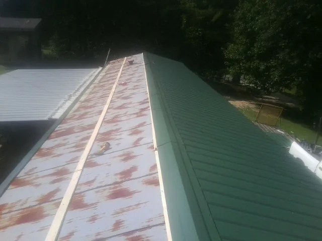 Old rusted panels beside newly installed green metal roofing — Wind Damage Roof Repair by Roofing Brothers in Gold Creek