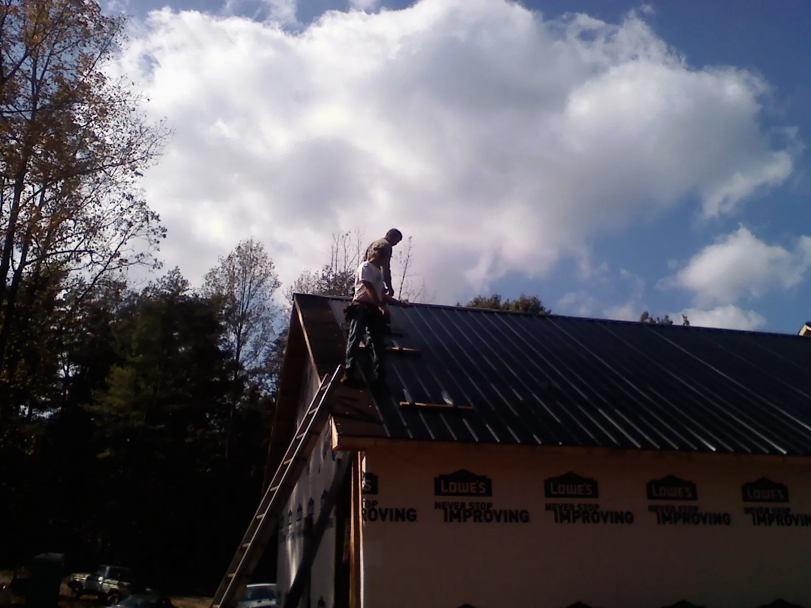 Roofer fastening dark metal panels high against a cloudy sky, from a Roof Inspection job in Gold Creek