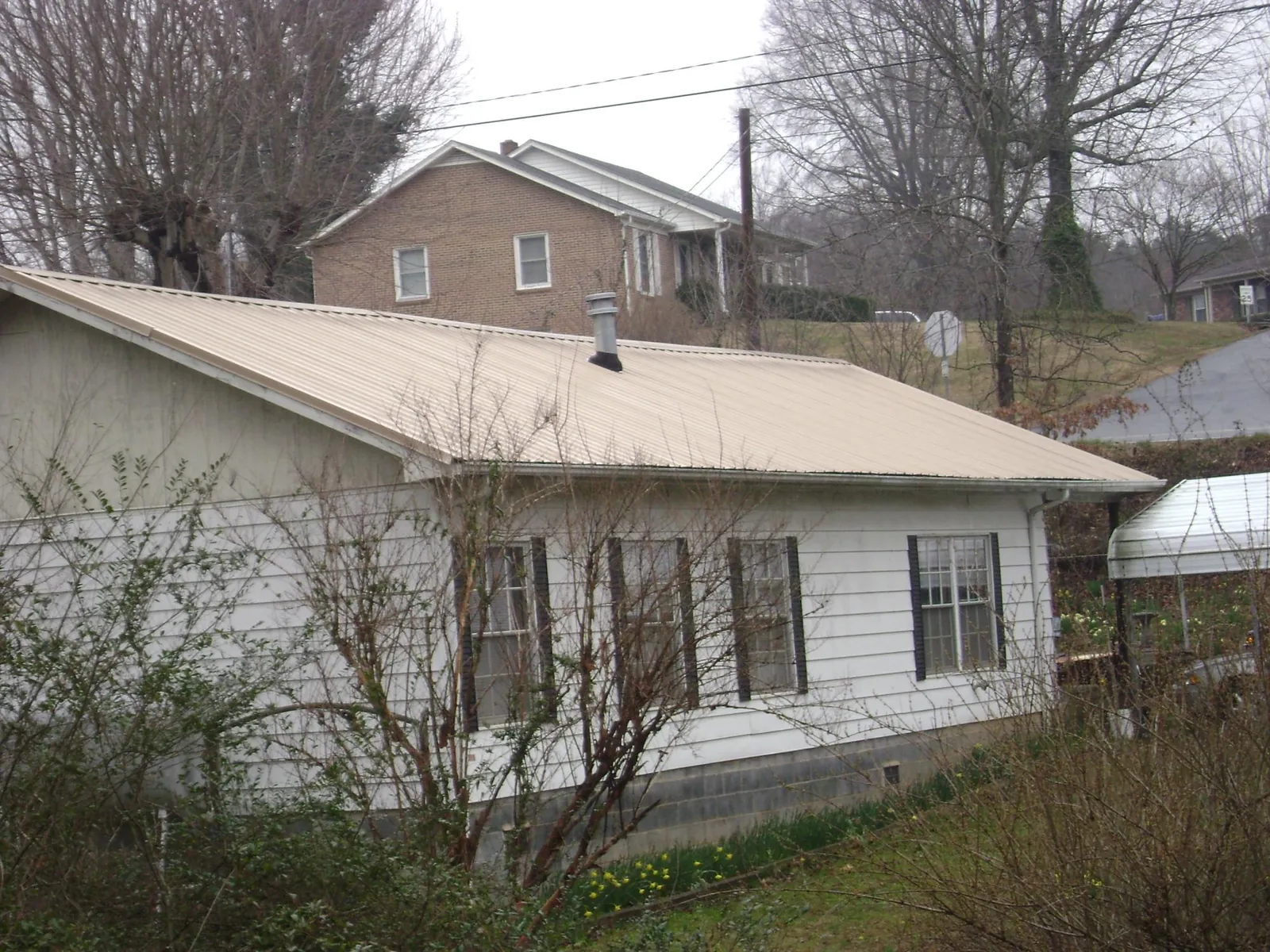 Tan metal roof on a white sided house set into a hillside — Commercial Roofing by Roofing Brothers in Gold Creek