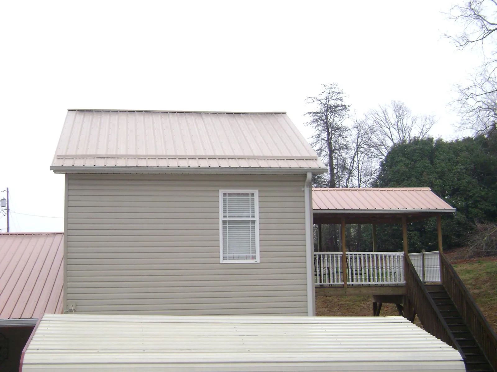 Tan metal roofs on a two story addition and attached porch, from a Roof Replacement job in Gold Creek